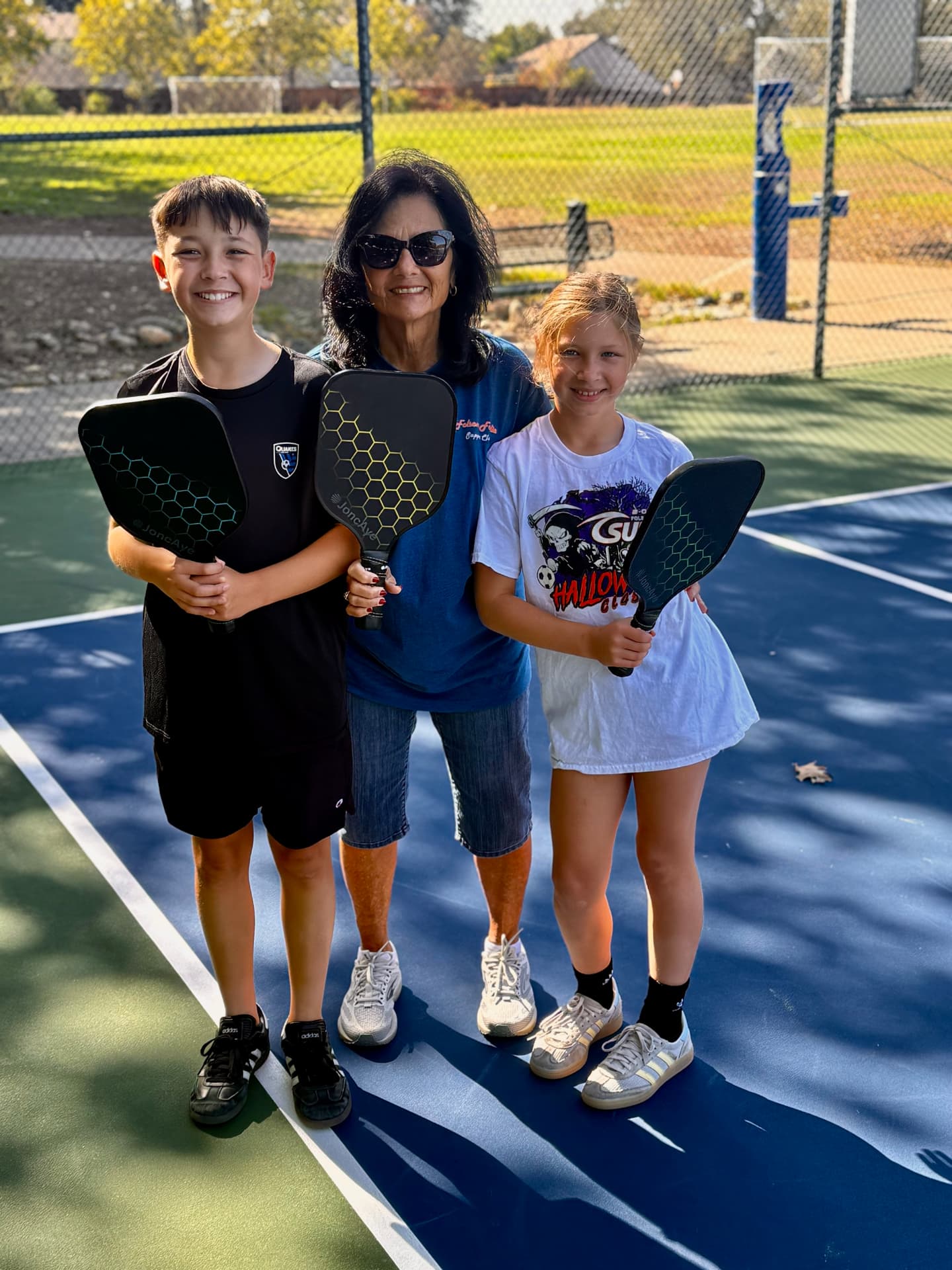 Walter, Grandma Marie, and Ruby holding pickleball paddles on an outdoor court
